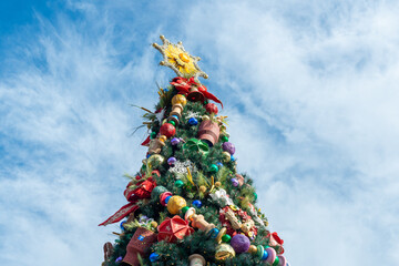 A large tree is displayed outside and covered in gold sparking garland, silver and gold balls, rhinestone feathers, and glitter. The Christmas tree sparkles with glass baubles and a large glass topper