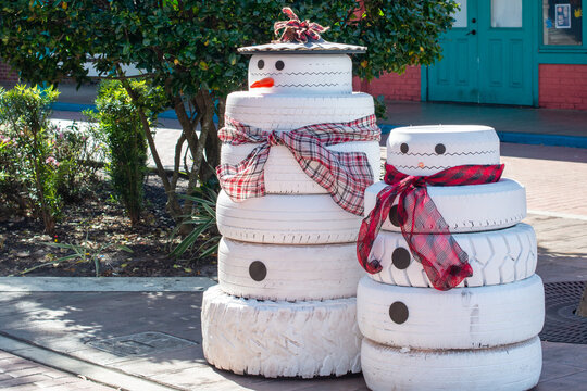 Homemade Christmas snowmen on display. The recycled tires are painted white with black buttons. Both lawn ornaments have scarfs wrapped around the decoration and the taller snowman is wearing a hat.