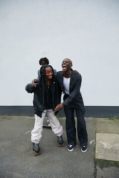 Young black girl wearing rollerskates holds on to her fashionable friend to stop herself from falling