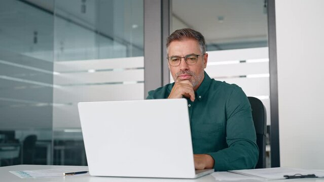 Busy middle aged professional business man working on laptop at office desk. Older serious male entrepreneur typing on computer, executive manager investor analyzing digital financial market in office