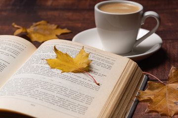 Naklejka na ściany i meble Autumn leaves, cup of coffee and open book on wooden table, autumn reading, cozy home