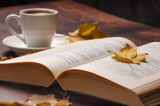 Autumn leaves, cup of coffee and open book on wooden table, autumn reading, cozy home