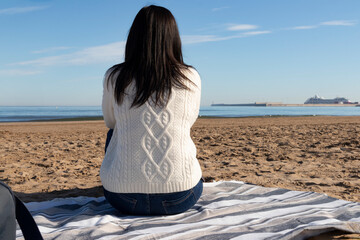 girl from behind sitting on the beach admiring the sea