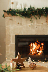 Stylish christmas wooden trees, star, pine cones and fir branches on table against burning...