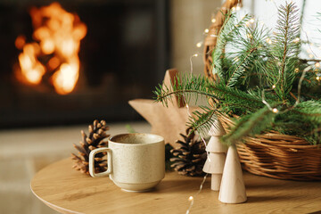 Winter cozy living room in farmhouse. Stylish cup of warm tea, basket with fir branches, wooden...