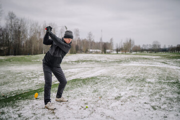 A man makes a shot with a club on the golf course in winter