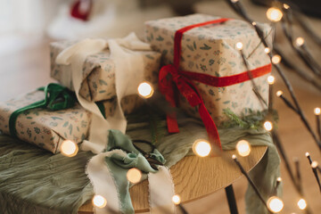 Stylish wrapped christmas gifts with ribbons and scissors on table with festive golden lights. Merry Christmas and Happy Holidays! Modern presents, atmospheric christmas eve