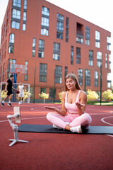 Fitness Vlog. Portrait of active smiling woman filming video for her internet channel at social media, using smartphone on tripod, trainer recording tutorial on the basketball court