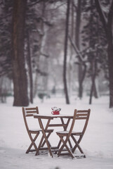 Christmas outdoor terrace with table, chairs and Christmas decorations and lights. a snowy winter street scene. Christmas cafe with wooden table, chairs and Red cup with spruce branches and red berry.