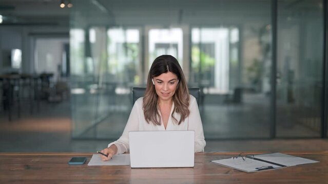 Happy professional mature female hr manager, smiling mature mid aged business woman in office wearing earbud looking at laptop computer having hybrid conference work meeting or remote job interview.