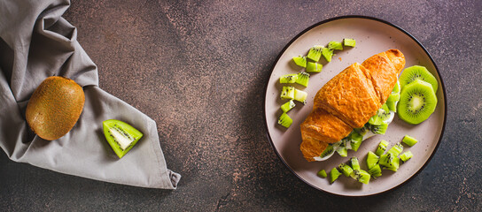 Croissant sandwich kiwi fruit and yogurt on a plate on the table top view web banner