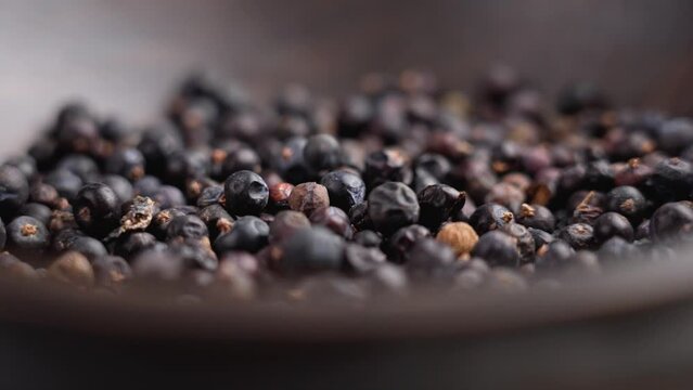 Dried juniper berries falling into a dark wooden bowl close up. Natural seasoning. Rotation. Macro shot