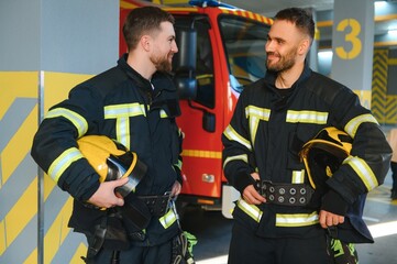 Fototapeta premium Two firefighters in protective clothing in helmets with fire engine