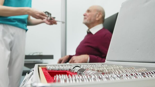 Close-up of glasses for trial optometry in the hands of an ophthalmologist, with an elderly patient sitting in the background. An ophthalmologist checks a man's vision in the hospital.