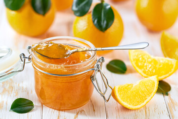 Spoon with delicious orange marmalade or jam over jar on table. Space for text.