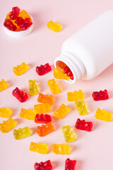 Group of gummy supplements with multivitamins and a bottle for them on a pink vertical view