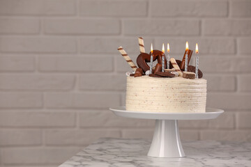 Delicious cake decorated with sweets and burning candles on white marble table, space for text
