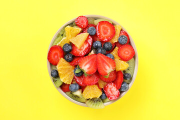Yummy fruit salad in bowl on yellow background, top view