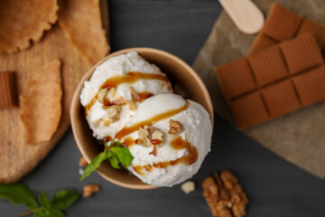 Tasty ice cream with caramel sauce, mint and nuts in paper cup on grey table, flat lay