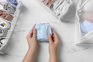 Woman folding panties at white marble table with organizers of underwear, top view