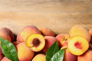 Cut and whole fresh ripe peaches with green leaves on wooden table, flat lay. Space for text