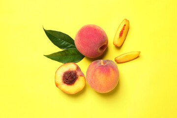 Delicious juicy peaches and green leaves on yellow background, flat lay