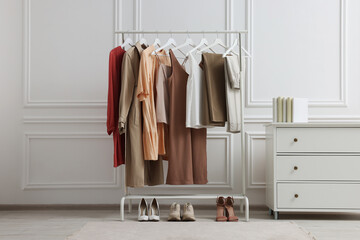 Rack with different stylish women`s clothes, shoes and dresser near white wall in room