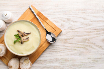 Bowl of tasty cream soup with mushrooms, parsley and spoon on light wooden table, flat lay. Space for text