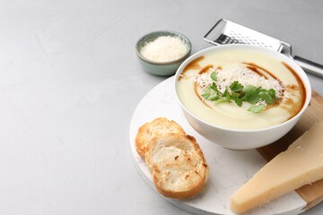 Delicious cream soup with parmesan cheese, soy sauce in bowl and croutons on light grey table. Space for text
