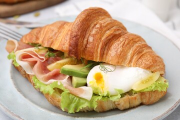 Delicious croissant with prosciutto, avocado and egg on white table, closeup