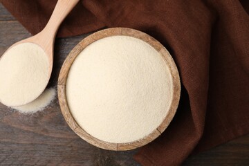 Uncooked organic semolina in bowl and spoon on wooden table, top view