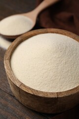 Uncooked organic semolina in bowl and spoon on wooden table, closeup