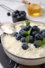 Bowl of delicious rice porridge with blueberries and mint on table, closeup