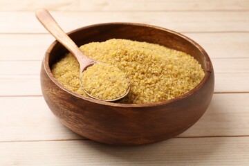 Bowl and spoon with raw bulgur on light wooden table
