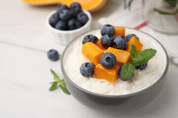Bowl of delicious rice porridge with blueberries, pumpkin and mint on white table, closeup