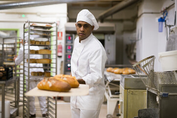 Male baker pulls hot bread out of the oven at the bakery