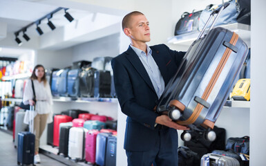 Positive male customer choosing travel suitcase in haberdashery shop