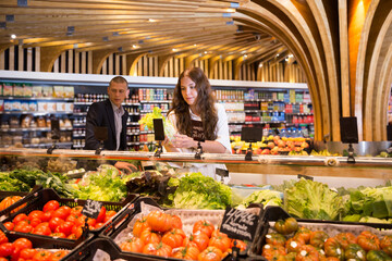 Young woman searching for fresh greens while shopping in greengrocery section at supermarket