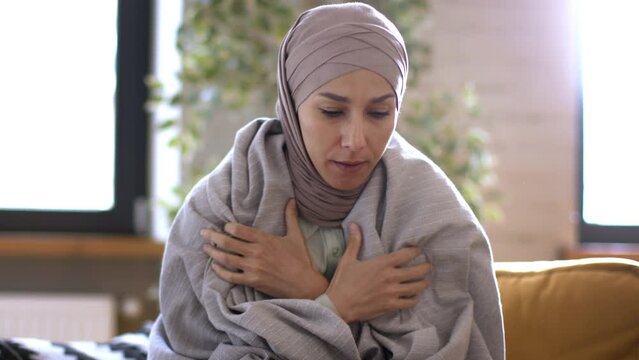 Heating problem. Young unhappy muslim woman freezing at home, wrapping herself in plaid and warming hands, tracking shot