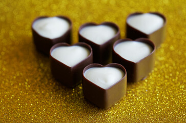 Heart-shaped chocolates made from dark and white Belgian chocolate. Festive golden background. Photo. Bokeh. Selective focus.