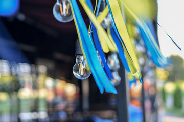 Flattering blue and yellow ribbons hanging with retro light bulbs string. Selective focus. Low DOF.