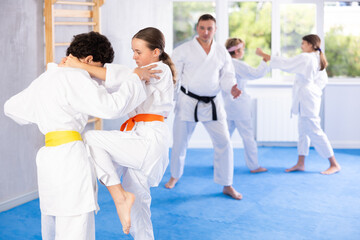Fototapeta na wymiar Girl and boy in kimono sparring together in gym during karate training
