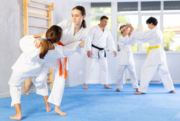 Two girls in kimonos train judo techniques in group in studio