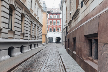 Fototapeta premium Empty street with cobble stone floor in the ancient neighbourhood in Riga, Latvia on a grey autumn day