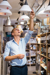 European man choosing lamps in store. He's looking upward and touching lamp shade.