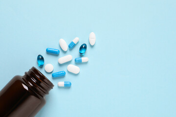 Plastic bottle with many different pills on light blue background, flat lay. Space for text