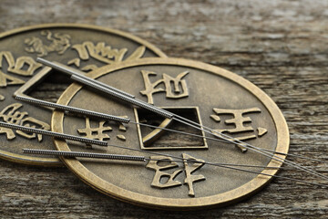 Acupuncture needles and ancient coins on wooden table, closeup