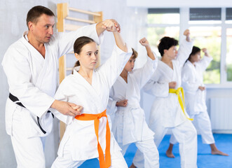 Fototapeta na wymiar Karate card training class for children with experienced trainer, black belt in martial arts. Teacher corrects pose posture position of body, hands, legs during karate classes.