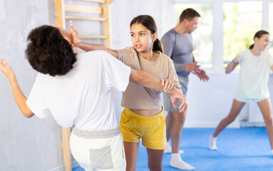 Girls and boys practicing in pair self-defence movements with female trainer supervision