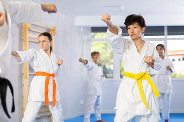 Fototapeta na wymiar Group of preteen children in kimono trying new martial moves at karate class